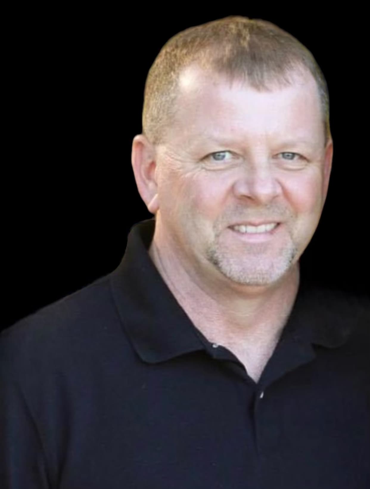 Smiling middle-aged man with short brown hair and a goatee wearing a black polo shirt.