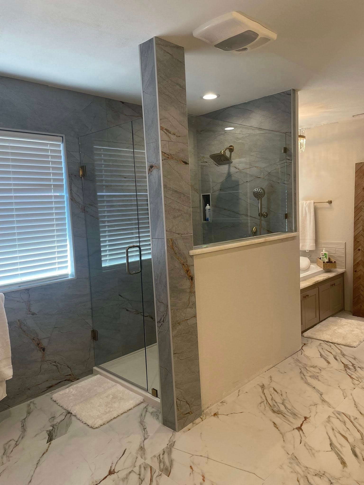 Modern bathroom with grey marble shower walls, gold fixtures, glass door, and white marble floors.